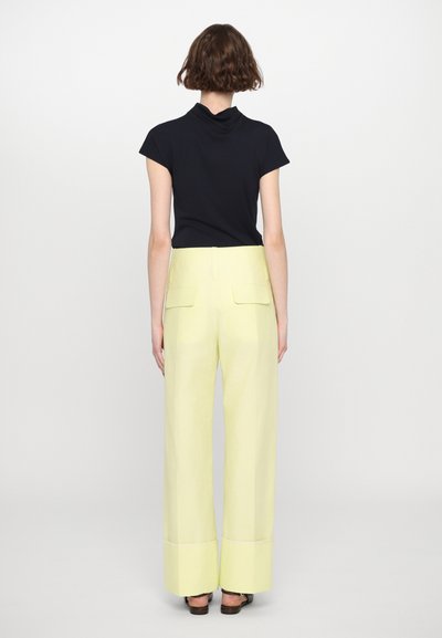 Haut noir à manches courtes associé à un pantalon large jaune pâle avec poches arrière et poignets contrastants. Texture lisse, coupe décontractée.