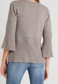 Grå stickad tröja med klockformade ärmar, texturerad vävd kropp och slät ovandel, tillsammans med ljusblå denimjeans.