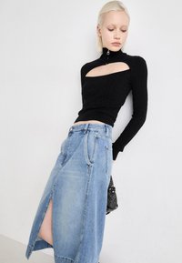 Svartstrikket topp med høy krage og utskåret detalj, kombinert med en lys blå denimskjørt med frontslitt og lommer.