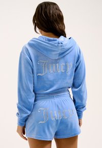 Light blue velour tracksuit featuring a hooded top and matching shorts. Decorated with rhinestone "Juicy" text on both pieces.