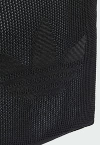 Černá síťová taška s výrazným černým logem listu, vyrobená z texturované látky s tkaným vzorem a hladkými akcenty.