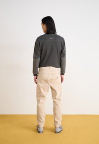 Haut à manches longues gris foncé avec des détails cousus et pantalon beige clair ample. L'ensemble comprend des poches et une étiquette de logo visible.