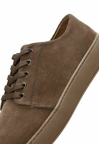 Basket basse en daim marron avec des lacets marron et une semelle épaisse en caoutchouc, vue en gros plan sous un angle.