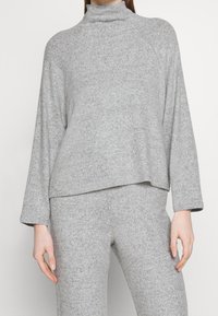 Szary golf wykonany z miękkiego materiału, cechujący się luźnym krojem, długimi rękawami i lekko wydłużonym dołem, co nadaje warstwowy wygląd.