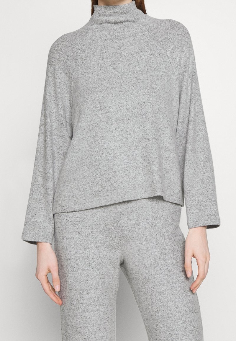 Szary golf wykonany z miękkiego materiału, cechujący się luźnym krojem, długimi rękawami i lekko wydłużonym dołem, co nadaje warstwowy wygląd.