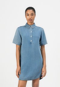 Lys blå denimskjortekjole med kort erme, krage og knappelukking. Har kontrastsøm og en avslappet passform.