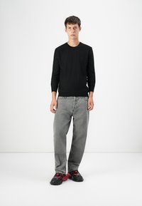 Top lung cu maneci lungi de culoare neagră, blugi gri și încălțăminte neagră și roșie. Croială slim, textură ribbed pe top, croială relaxată pentru blugi. Fundal simplu.