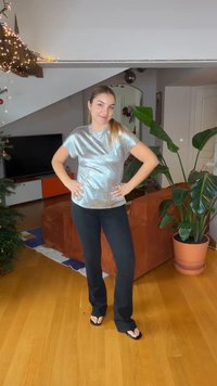 Shiny silver short-sleeve top, relaxed fit; paired with black flared pants and simple black flip-flops, standing in a bright room.