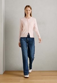 Light pink cardigan with long sleeves, round neckline, and front buttons, paired with high-waisted blue jeans and white shoes.