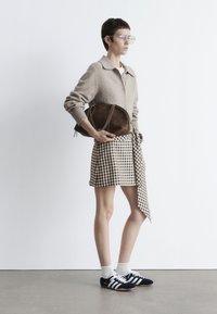 Hellbrauner Wollcardigan, karierten beigen Rock mit seitlichem Bindeband und marineblaue Sneaker mit weißen Streifen. Passende braune Wildledertasche.