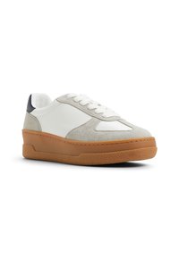 Białe skórzane i szare zamszowe sneakersy z masywną brązową gumową podeszwą i okrągłym noskiem, z sznurowaniem z przodu i granatowym akcentem na pięcie.