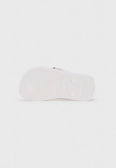 Bela gumijasta podplat sandal z teksturiranimi vdolbinami, dvema okroglicama in delom za blagovno znamko. Ploski dizajn brez dviga pete.