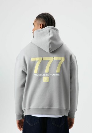 Grijze hoodie met een groot geel nummer "777" en tekst "WORLD IS YOURS" op de achterkant. Voorzien van een capuchon met trekkoorden en geribbelde zoom.