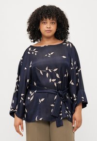 Blusa navy a vestibilità ampia, con un motivo floreale in beige chiaro, scollatura ampia e un accento in vita legato. Le maniche svasate completano il design.