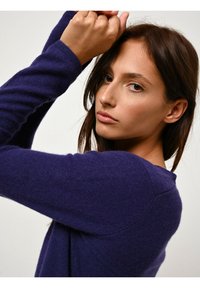 Maglione viola a maglia con maniche lunghe e scollatura rotonda. Texture morbida, design aderente. Dettagli di cucitura sottili lungo le spalle.