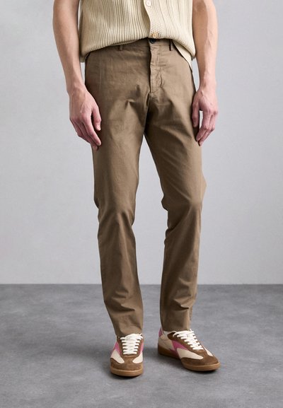 Světle hnědé chinos kalhoty s rovnými nohavicemi, které mají boční kapsy a hladkou texturu, zkombinované s vícebarevnými retro teniskami na tkaničky.