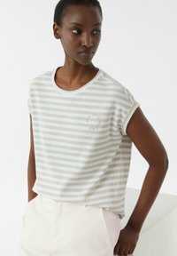 Gestreiftes Kurzarm-T-Shirt in Beige und Hellblau, mit Rundhalsausschnitt und einem kleinen runden Logo-Detail auf der Brust.
