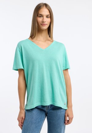 Licht teal V-hals T-shirt met korte mouwen, zachte textuur, relaxte pasvorm en een klein accentlogo aan de zoom. Gecombineerd met blauwe jeans.