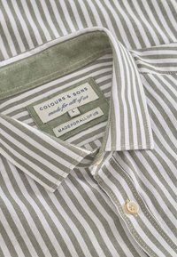 Camicia a righe con sottili righe verdi e bianche, colletto button-down e rinforzo del colletto di un verde chiaro. L'etichetta riporta "Colours & Sons," taglia L.