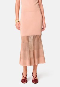 Gebreide kokerrok in lichtbeige met een uitlopende, geribde zoom. Gemaakt van zacht materiaal met transparante horizontale panelen. Gecombineerd met rode sandalen met bandjes.