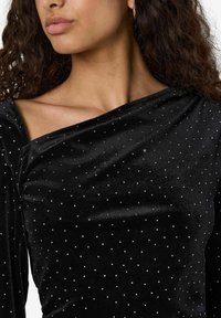 Svart fløyels-topp med off-shoulder-design, med en glatt tekstur og spredte sølvfargede rhinestones som pynt.