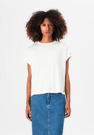 T-shirt blanc à manches courtes avec un col rond, coupe fluide et petit logo brodé à l'ourlet, associé à une jupe en denim.