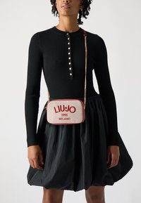 Torba preko ramena od bež tkanine, s crvenim vezom "LIUJO 1995 MILANO", zlatnom lancem i strukturiranim pravokutnim oblikom.