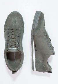 Olivgröna kanvas sneakers med grå detaljer, snörningsdesign, gummisula och kontrasterande sömmar. Inkluderar logotypdetalj på sidan.