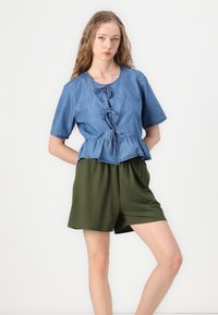 Denim peplum top s krátkymi rukávmi, s viazaným predným dielom a olivovo zelenými elastickými šortkami. Hladké textúry a ležérny dizajn.