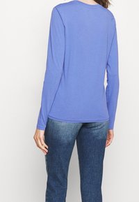 Chemise violette à manches longues en tissu doux, avec un col rond et une coupe décontractée, associée à un jean denim bleu.