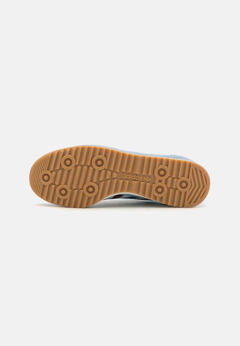 Suela de zapatilla Adidas con una superficie de goma textura, que presenta patrones de agarre circulares y un logo grabado cerca del área del talón.
