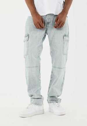 Pantalones cargo azul claro de mezclilla con múltiples bolsillos, un ajuste holgado y un ligero desgaste. Combinados con zapatillas blancas.