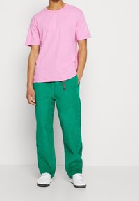 Rosa bomullströja med rund halsringning, som kombineras med löst sittande gröna byxor med dragsko. Vita sneakers fulländar outfiten.