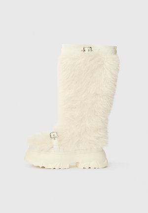 Knee-high cream faux fur boot with a chunky white rubber sole, featuring a buckle strap and flat, textured design.