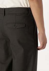 Charcoal gray trousers with a smooth texture, featuring a rear pocket with a black button and a side pocket, tailored fit.