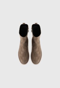 Botas de tobillo de ante marrón con una textura suave, puntera redonda y diseño minimalista. Cuentan con una cremallera trasera y una lengüeta corta para facilitar el calzado.