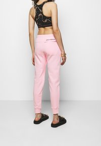 Svart blommig sportbh med bred resårband, tillsammans med ljusrosa joggerbyxor med bakdragkedja och logotypdetalj ovanför midjebandet.