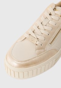 Sneaker beige con una toma in suede testurizzato, dettagli in pelle liscia, lacci piatti e una suola in gomma spessa con dettagli scanalati.