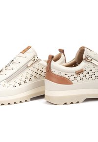 Baskets beige clair avec tige perforée et accents en cuir marron. Dotées de lacets et d'une fermeture éclair latérale, semelle en caoutchouc texturée avec un motif de bande de roulement.
