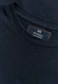 Tamsiai mėlynas apvalios apykaklės marškinėliai, pagaminti iš minkštos medvilnės. Ant tamsios fono yra etiketė su "Matinique" prekių ženklu ir "Heritage Apparel" balta spalva.