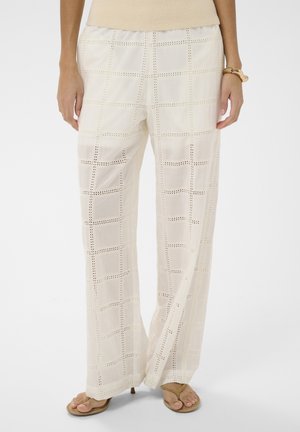 Weiße weite Hosen mit Gittermuster aus Lochstickerei, kombiniert mit beigem Oberteil und braunen Zehensandalen, Vorderansicht mit Beinen sichtbar.