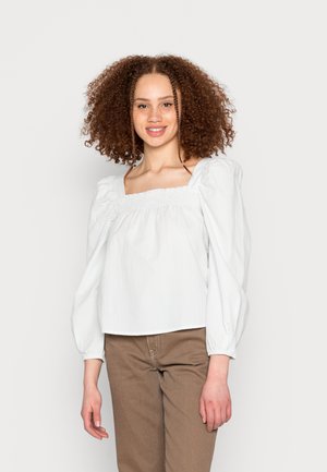 Blusa branca com riscas, de decote quadrado, mangas bufantes e um corte descontraído, combinada com calças castanhas. Textura suave, design casual.
