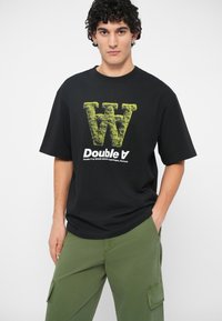 Črna kratka majica s kratkimi rokavi, ki na sprednji strani prikazuje velik, teksturiran, limetno zelen črko "W" in besedo "Double A" v krepkem belem fontu.