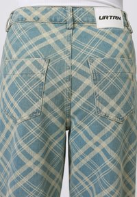 Blue plaid jeans with a light tan pattern, featuring a white label on the waistband and two back pockets. Textured denim finish.