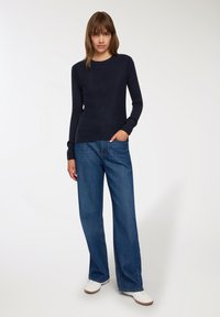 Granatowy sweter dzianinowy z długimi rękawami i ściągaczami, w połączeniu z szerokimi niebieskimi dżinsami i białymi trampkami. Gładka faktura i klasyczny design.