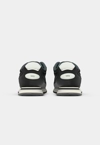 Zapatillas deportivas negras con una textura suave, detalles en blanco y un talón acolchado. Presentan la marca "1973" en los laterales.