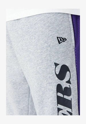 Pantaloni corti atletici grigi realizzati in tessuto morbido, con un grande logo nero, pannelli laterali in rete viola e un piccolo emblema del marchio.