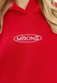 Czerwony hoodie z haftowanym słowem "MÍRONS" na białym tle, wykonany z miękkiego, teksturowanego materiału i z kapturem ze sznurkiem.