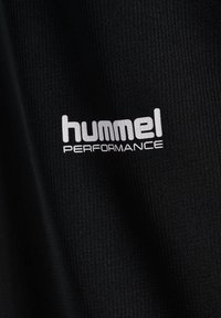 Sort stof med hvidt "hummel PERFORMANCE" logo trykt på tekstureret tekstiloverflade.