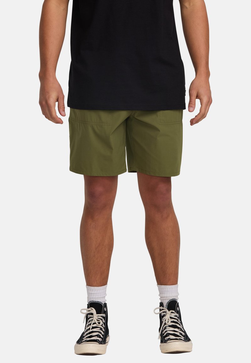 Pantalones cortos de color verde oliva con un ajuste regular, que presentan bolsillos laterales y una textura suave, combinados con zapatillas negras de caña alta y calcetines blancos.